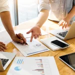 dos personas analizan un informe de marketing digital junto a varios dispositivos electrónicos