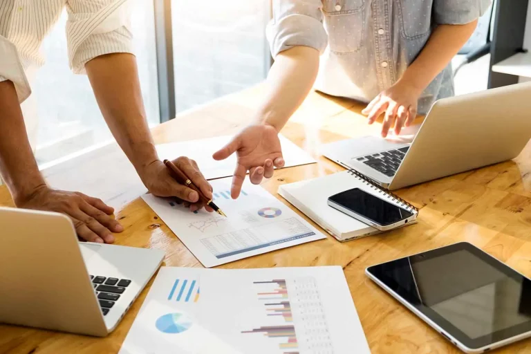 dos personas analizan un informe de marketing digital junto a varios dispositivos electrónicos
